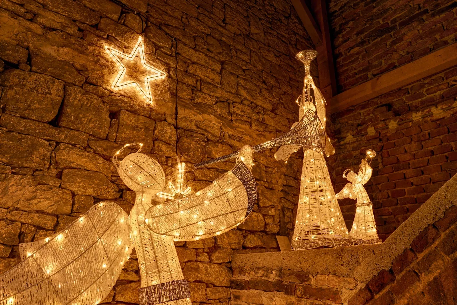 Warmweißer LED-Engel mit Trompete 122 cm neben einem leuchtenden Rentier und einem Bäumchen mit Sternen, Winterszene an einer Mauer